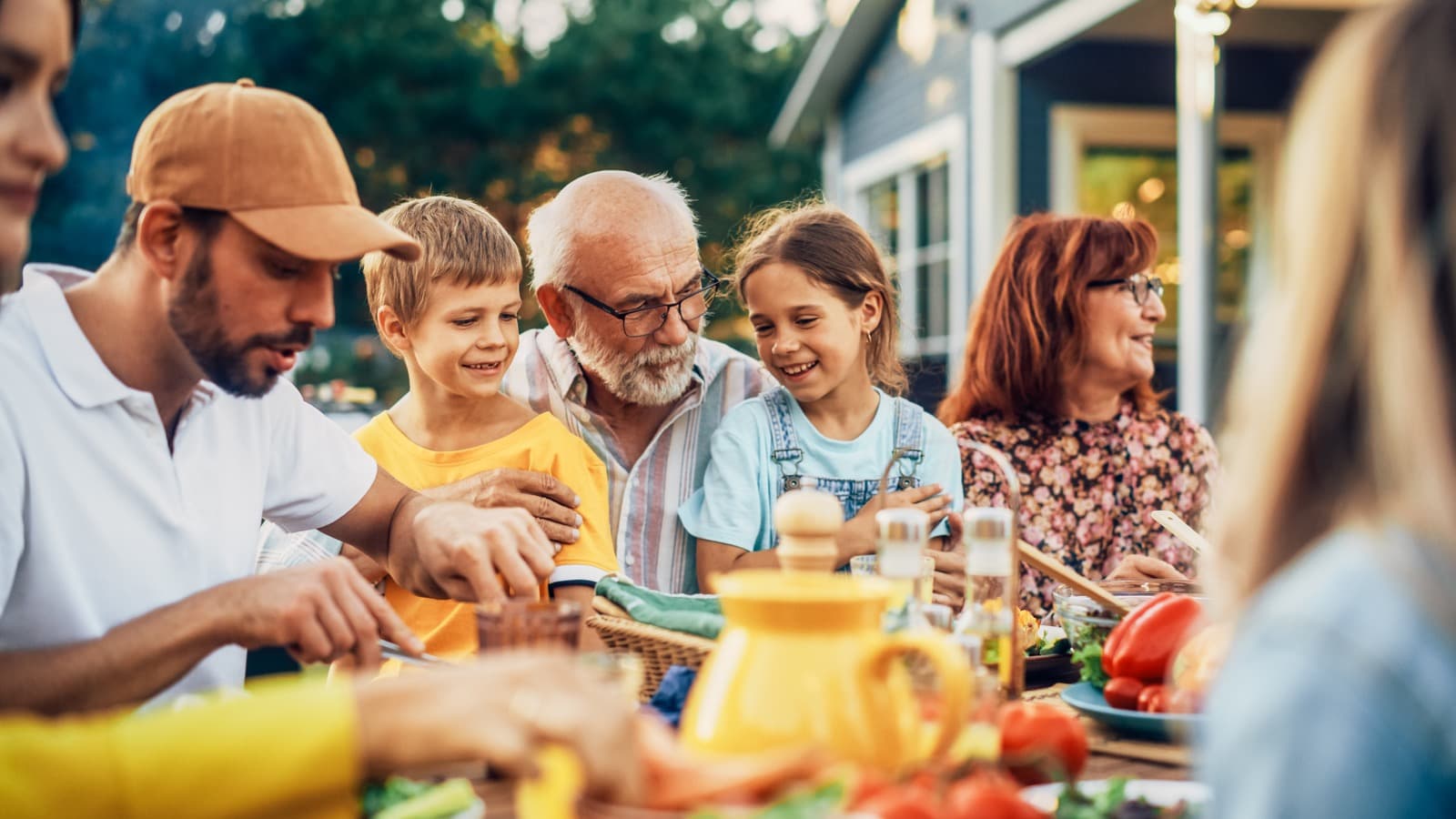 Happy grandfather holding his grandchildren on his lap at an outdoor family dinner
