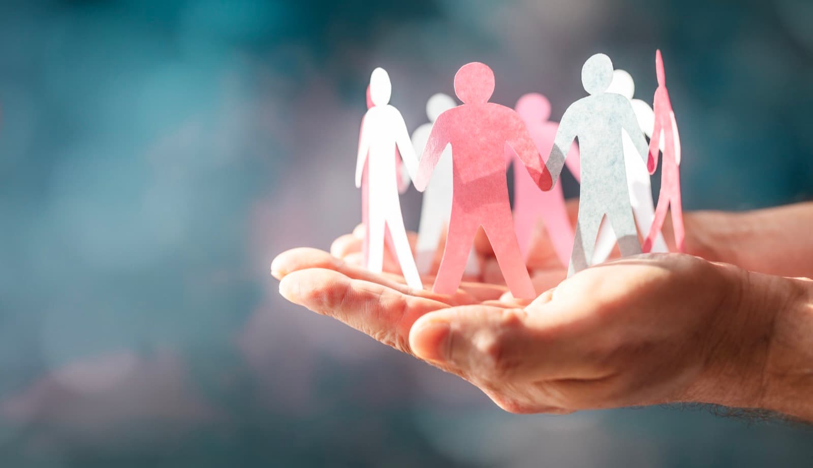 Cupped hands gently cradling a chain of paper people cutouts, symbolizing connected community support