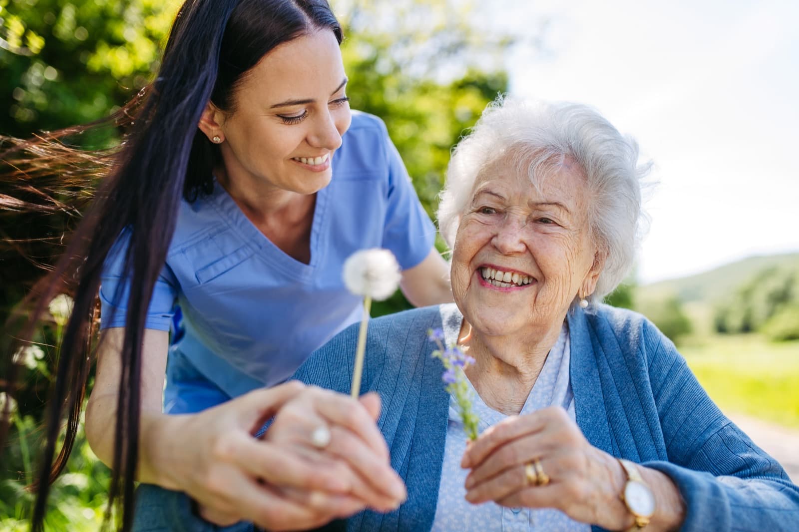 Young woman and older woman sharing a joyful moment outdoors with wildflowers in a sunny garden
