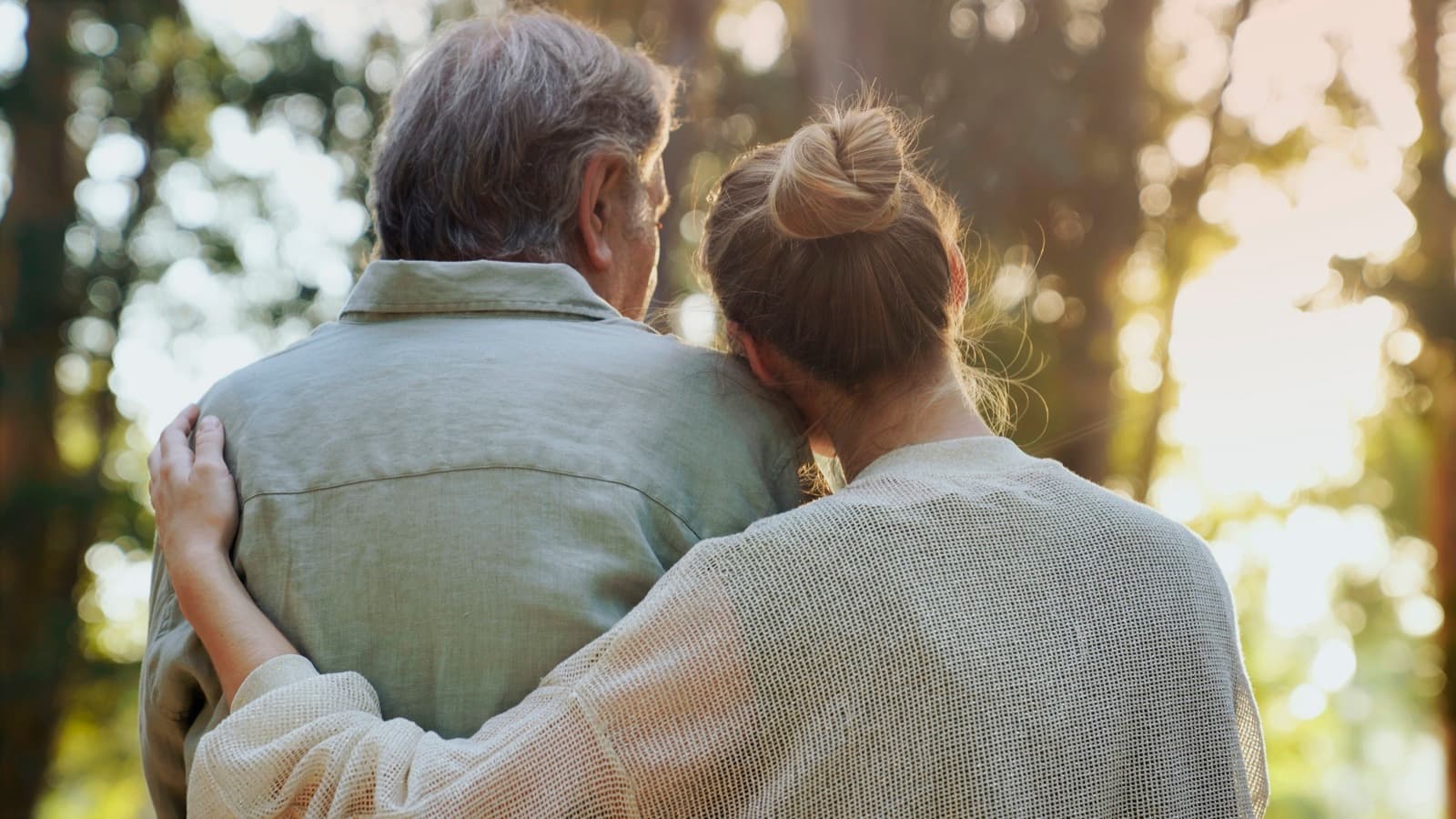 Adult daughter resting her head on her father's shoulder during a walk outdoors