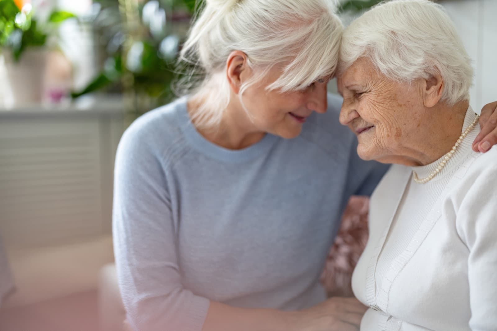 Senior woman and adult daughter sharing a warm moment with foreheads touching in a sunlit home